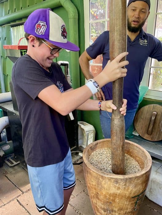 Amelie's son grinding grain with a giant wooden mortar and pestle